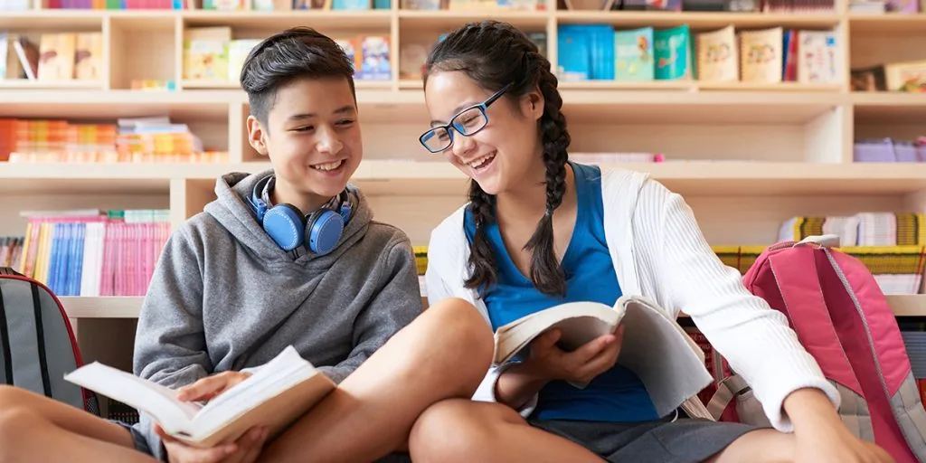Two students sitting together reading books in a school library