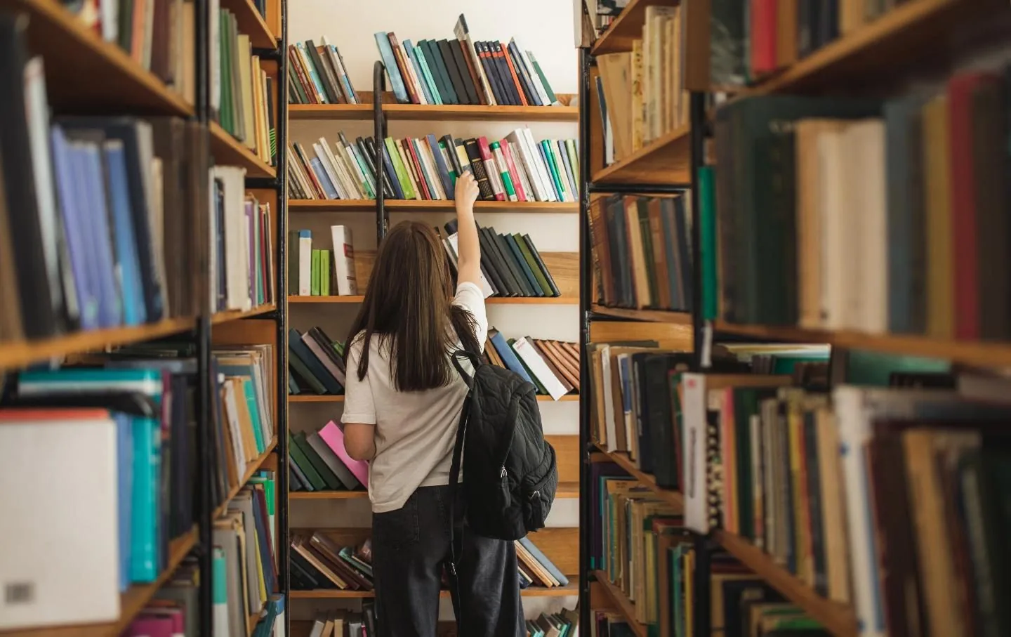 A student reaching for a book on a library shelf